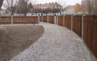 Erschließungsweg aus Natursteinpflaster, der durch eine mit Holzzäunen abgetrennte Gartenanlage führt