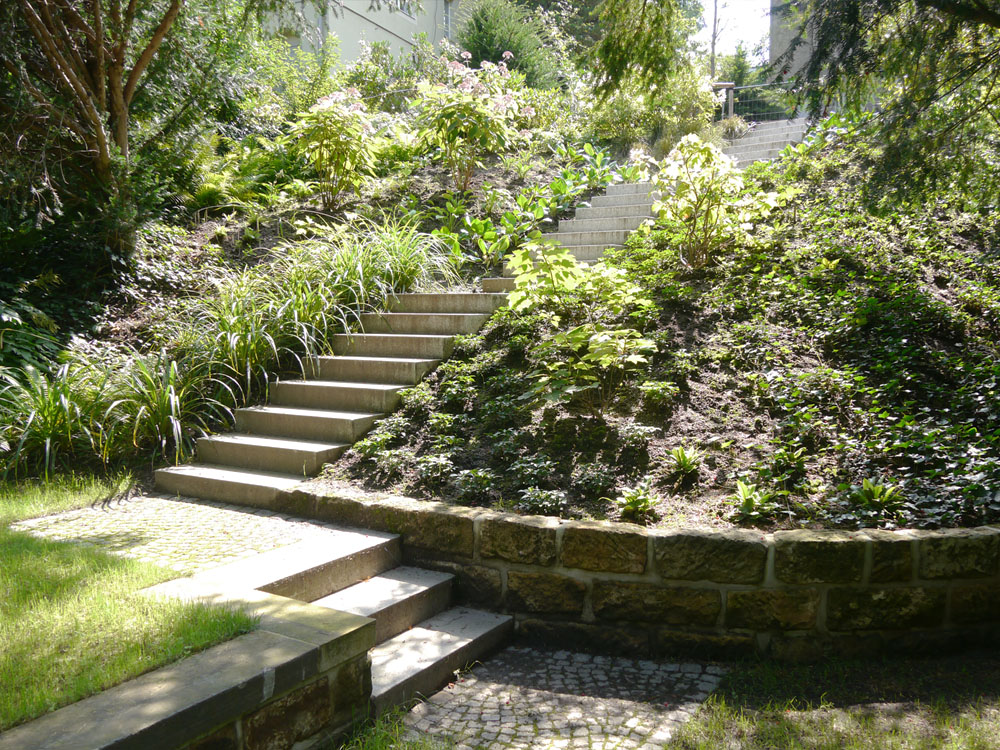 Blick vom unteren Gartenraum auf einen bepflanzten Hang mit einer Treppenanlage